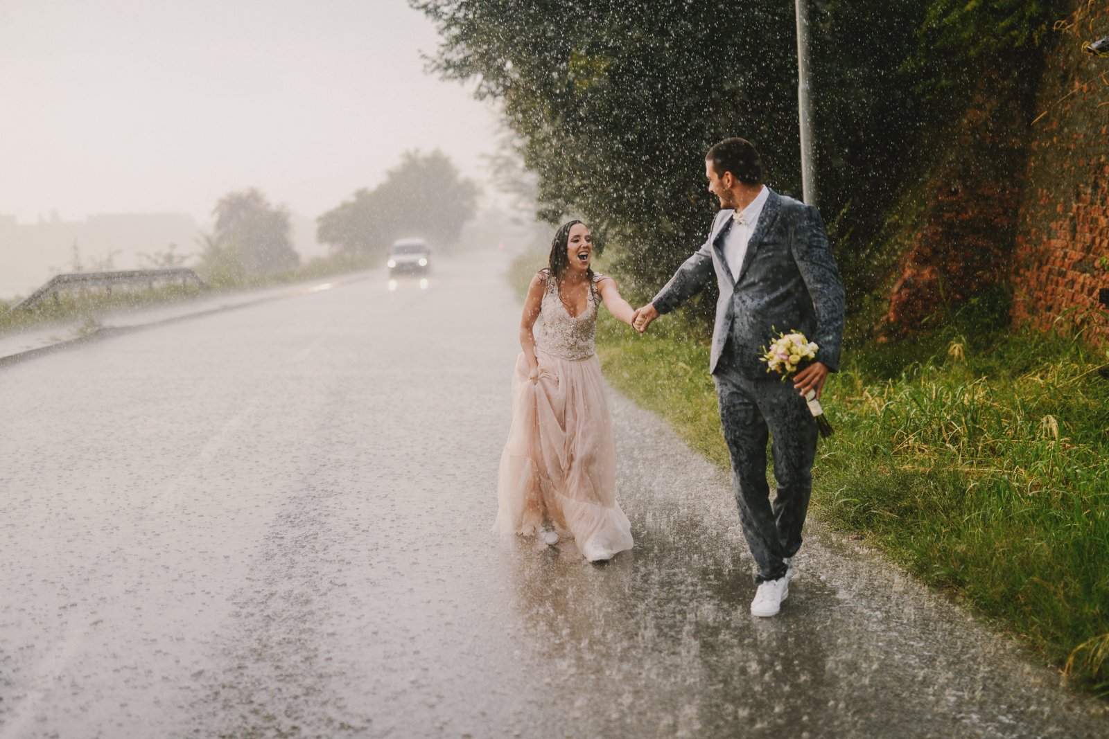 Couple holding hands in heavy rain, walking on the street and laughing.